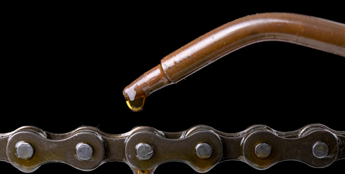 An oil nozzle is positioned above a chain. A drop of oil is coming out of the nozzle